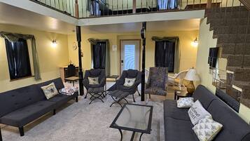 A spacious living area with a high ceiling, a staircase, and a balcony.