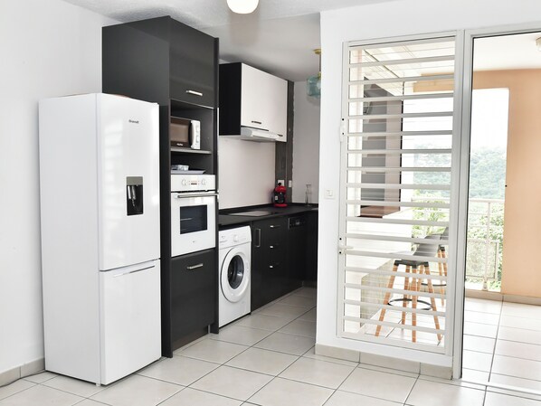 Une cuisine compacte équipée d’un réfrigérateur, d’un four, d’un four à micro-ondes et d’un lave-linge.