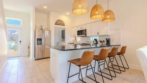 A modern kitchen with a central island, stainless steel appliances, and three wicker pendant lights. - The Flagship | Private Pool | BoardWalk|*GAME ROOM* (Port Aransas)