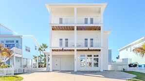 A two-story building with a garage, white exterior, and balconies. - The Flagship | Private Pool | BoardWalk|*GAME ROOM* (Port Aransas)