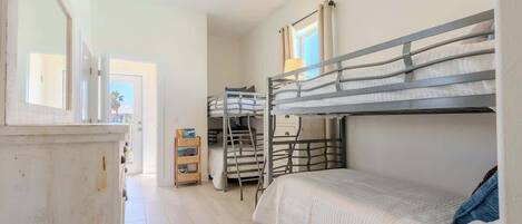 Een slaapkamer met een stapelbed, een raam, een klein houten kastje en een ladder.