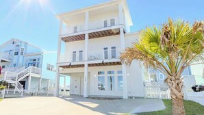 A multi-story beachfront house with a balcony, a staircase, and a palm tree in the foreground. - The Flagship | Private Pool | BoardWalk|*GAME ROOM* (Port Aransas)