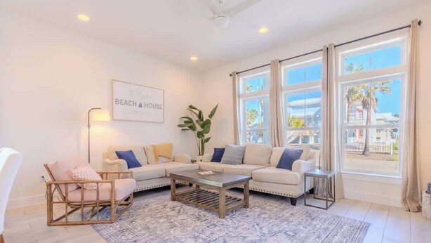 A living room with a sectional sofa, a coffee table, and a large window with curtains. - The Flagship | Private Pool | BoardWalk|*GAME ROOM* (Port Aransas)