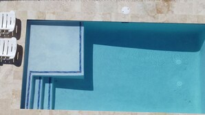 Ovenudblik over et rektangulært poolområde med fliseterrasse og to hvide liggestole.