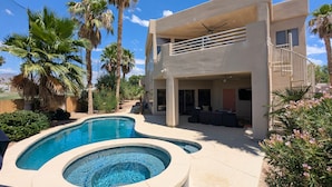 Une maison moderne à deux étages, dotée d’une piscine, d’un espace salon extérieur et de palmiers.