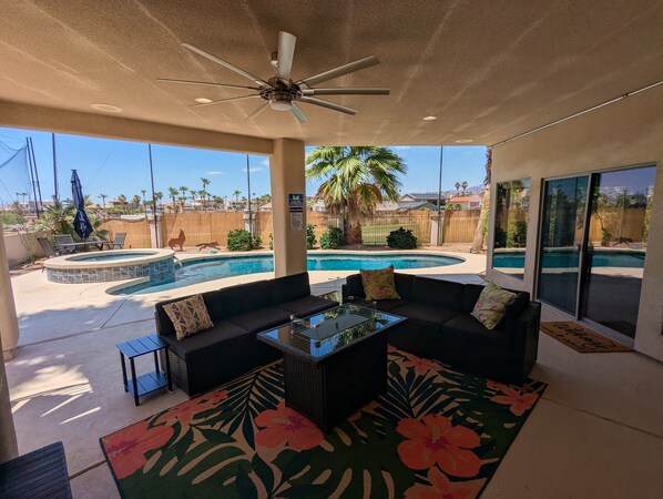 Un patio cubierto con piscina, mobiliario exterior y ventilador de techo.