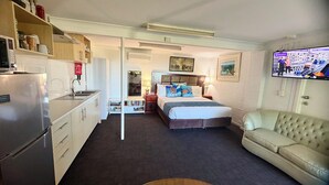 Een compacte hotelkamer met kitchenette, een bed met kussens met schildpadmotief, een televisie en een bank.