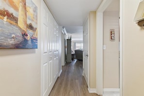 A hallway with white doors, a painting on the left wall, and a sign on the right wall.