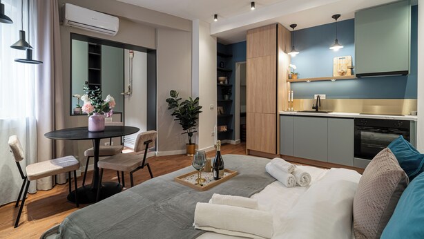 A modern hotel room with a bed, a dining table with chairs, a small kitchen area, and a large mirror. - Trendy & Private City Studios Near Cismigiu & Calea Victoriei (Bucharest)
