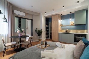 Ein modernes Hotelzimmer mit einem Bett, einem Esstisch mit Stühlen, einer kleinen Küchenzeile und einem großen Spiegel.