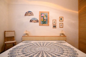 Une chambre Ă coucher comprenant un lit, une chaise, une table de chevet avec des lampes et des Ćuvres dâart accrochĂ©es au mur.