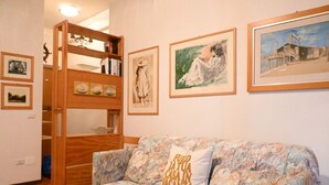 Een kamer met een bank met bloemenprint, een houten boekenkast en ingelijste kunstwerken aan de muur.