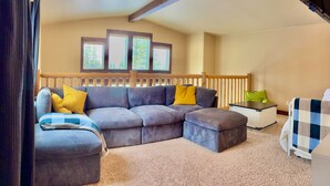 Una sala de estar acogedora con un sofá modular, una mesita y vistas a árboles a través de ventanas.