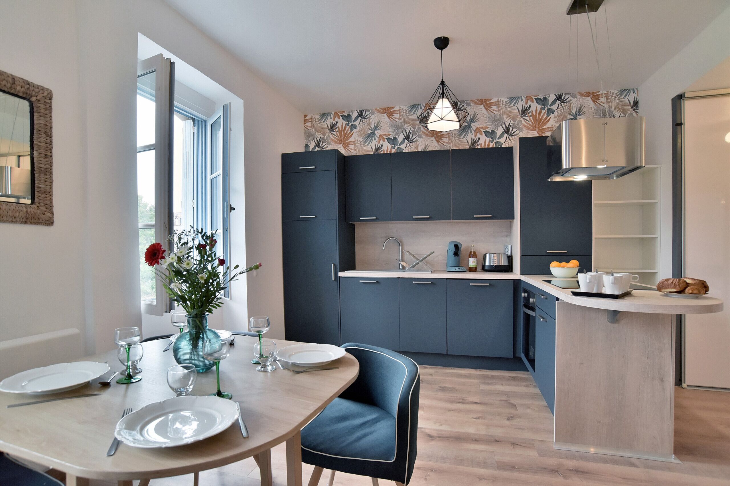 A modern kitchen with dark cabinets, a wooden dining table, and a vase with flowers.