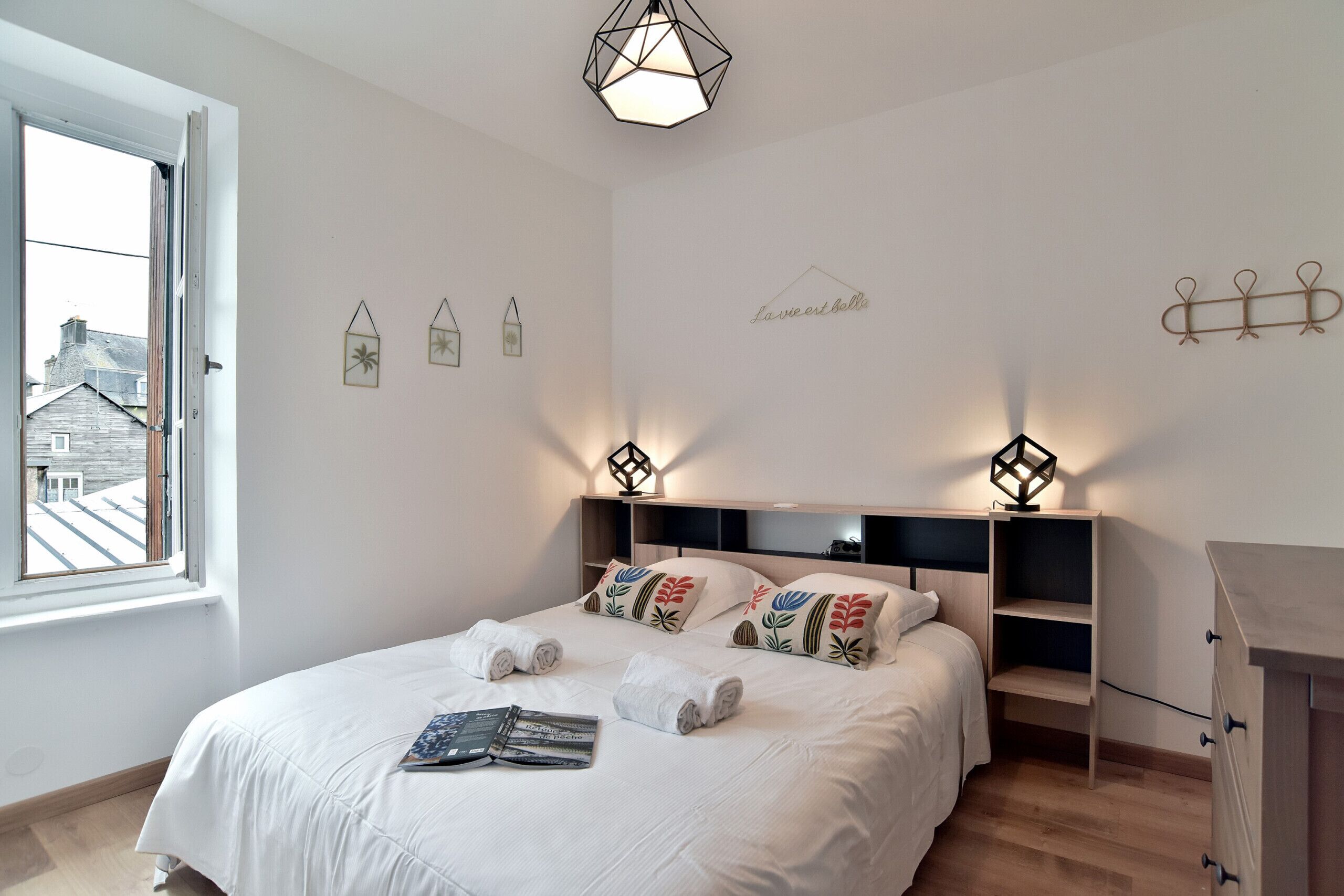 A bedroom with a large bed, bedside tables, a dresser, and a window with a view of buildings.