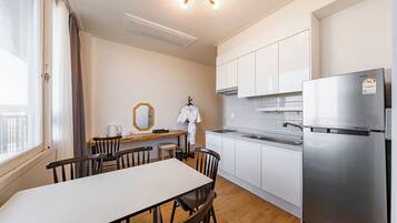 A compact kitchen with a stainless steel refrigerator, a dining table with chairs, and a window with curtains.