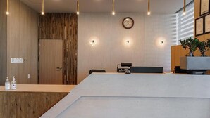 A reception desk with a wooden panel wall, a clock, and a plant on the right. - Incheon The Rest Hotel (Incheon)