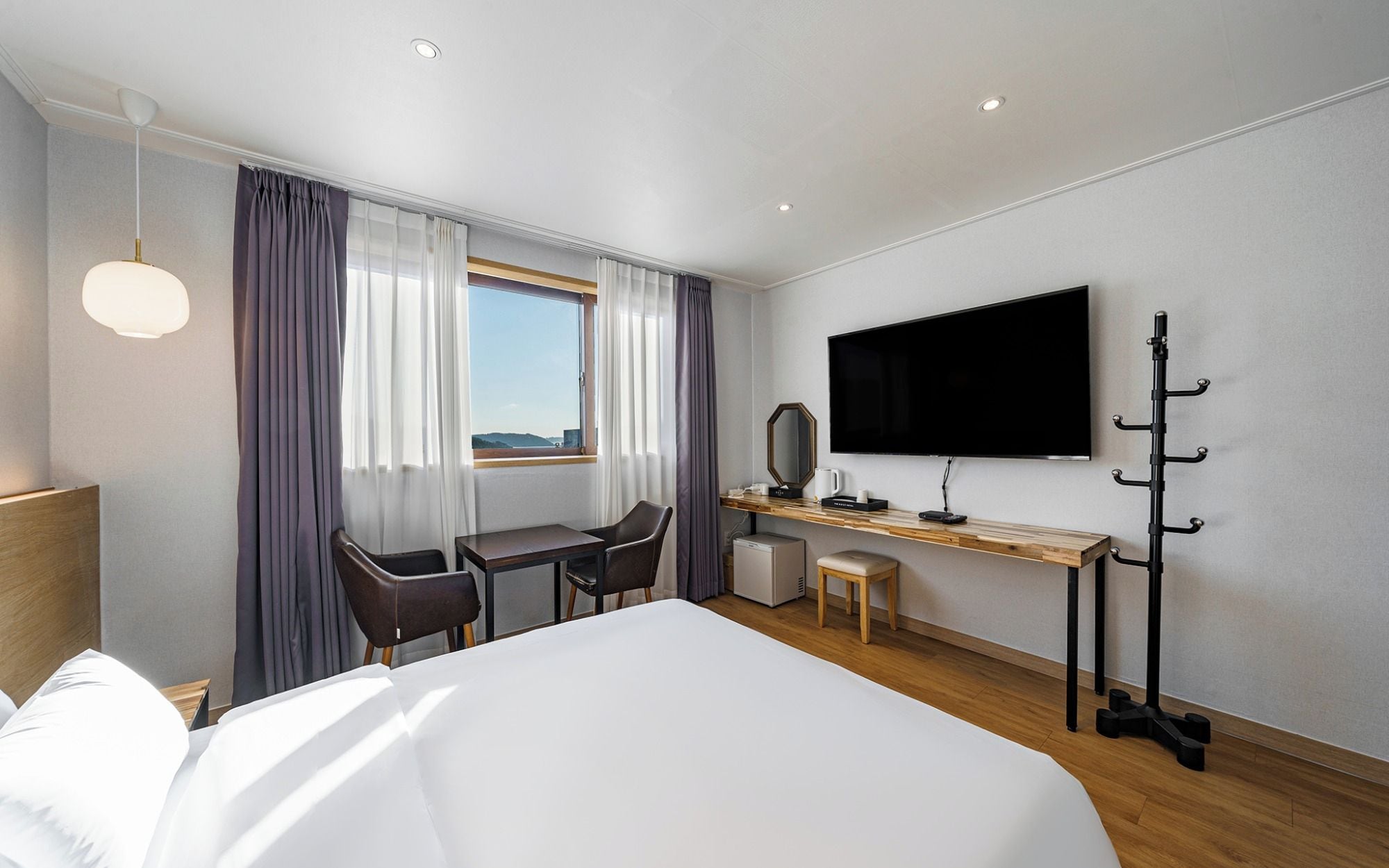 A hotel room with a large bed, a desk with a chair, a television, and a coat rack.