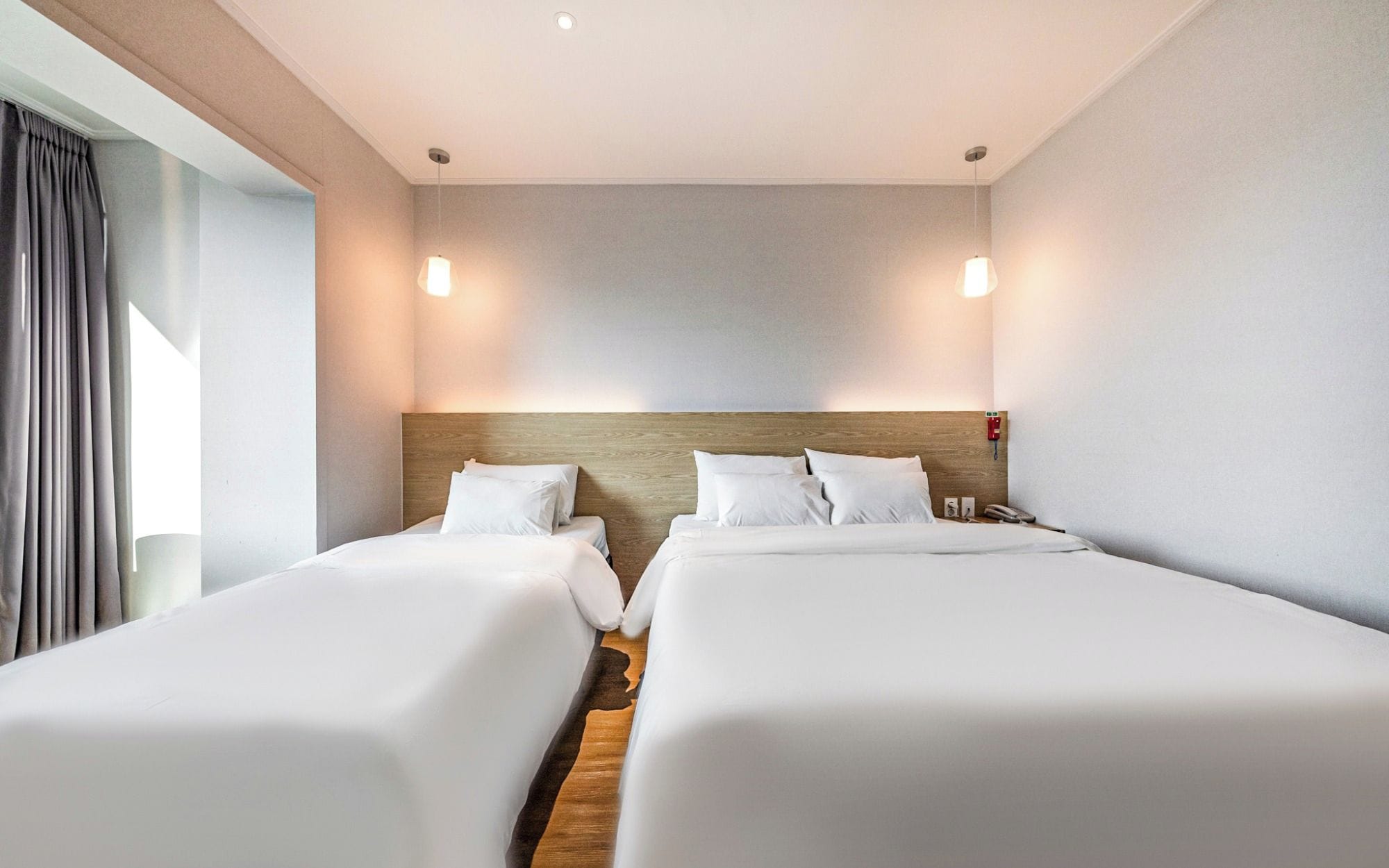 A hotel room with two beds, a wooden headboard, bedside tables, and a window with curtains.
