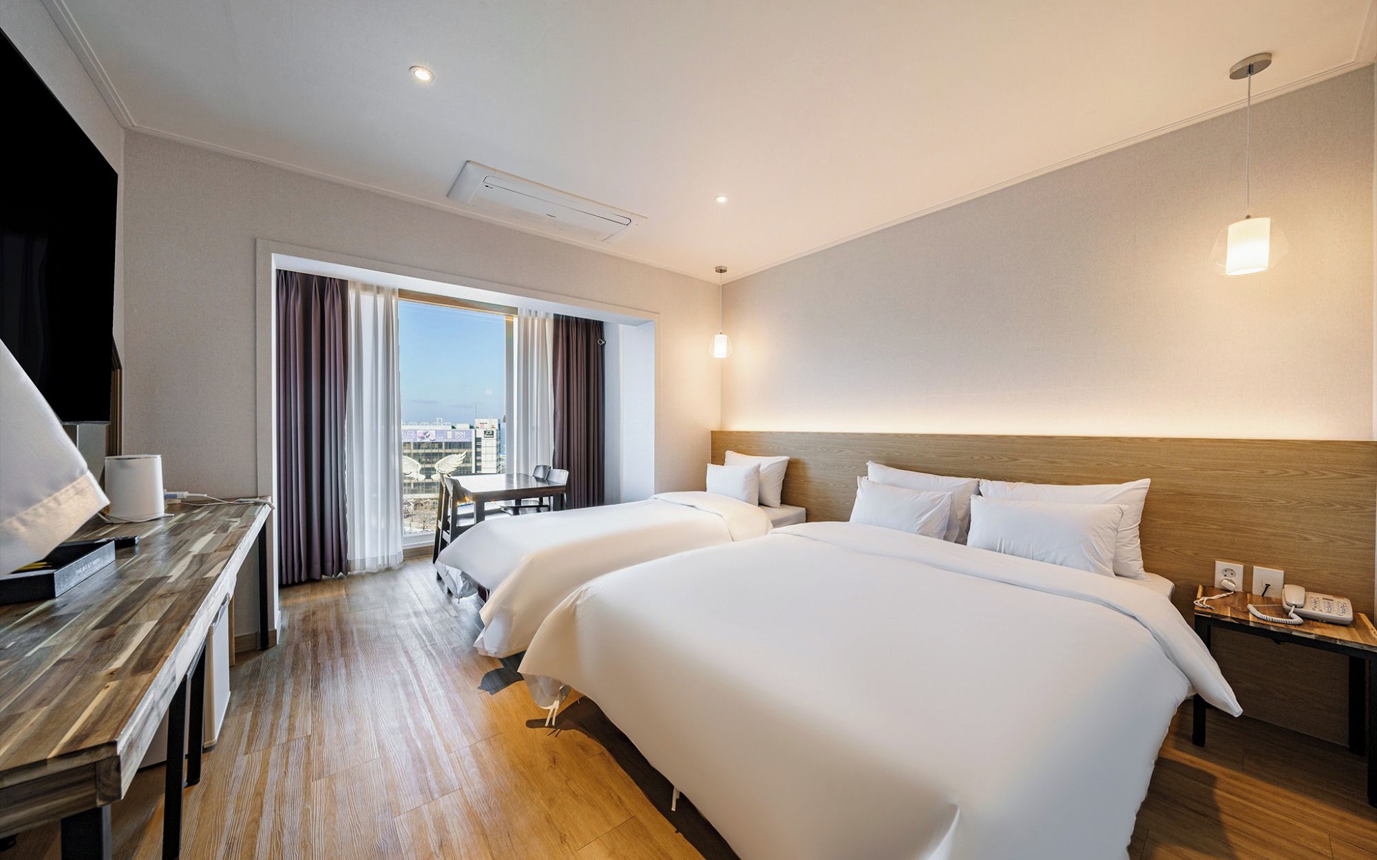 A hotel room with two beds, a desk, a chair, a telephone, and a window with curtains.