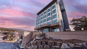 A multi-story hotel with a modern design, featuring a prominent entrance with a staircase, a parking area, and a view of the surrounding landscape. - Incheon The Rest Hotel (Incheon)