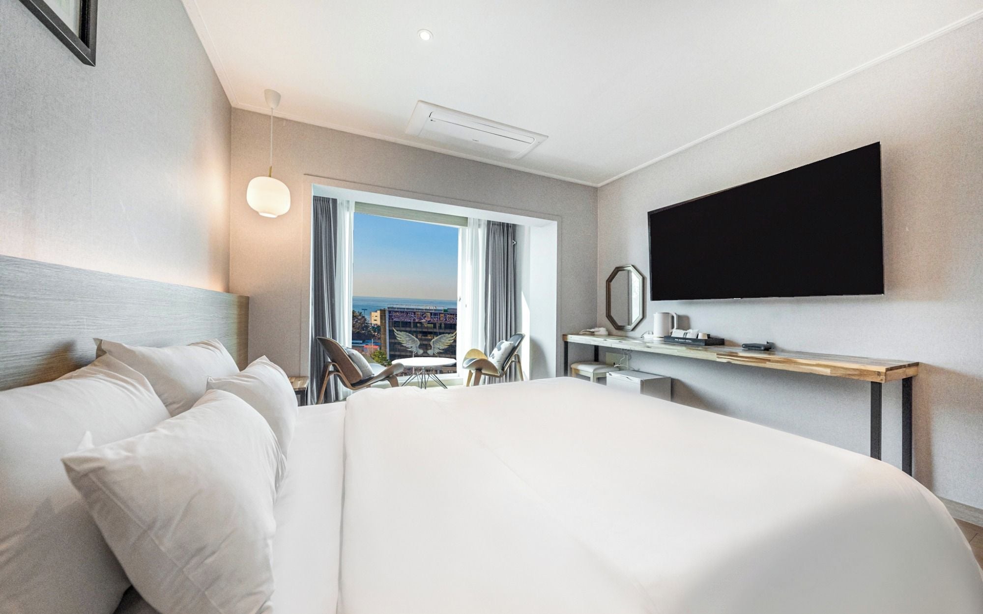 Habitación de hotel con una cama grande, un escritorio, un televisor de pantalla plana, una silla y vistas a la ciudad.