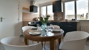 A modern kitchen with dark cabinets, a wooden countertop, and a window overlooking a cityscape. - La Plage du Petit Port (Cancale)
