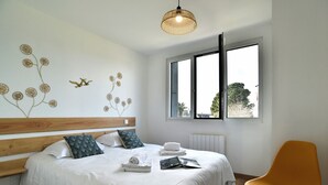 A bedroom with a bed, a wooden headboard, a window, a wall decoration, and a chair. - La Plage du Petit Port (Cancale)