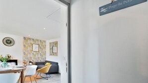 A modern interior with a dining area, a sofa, and a sign reading "Plage du Petit Port". - La Plage du Petit Port (Cancale)