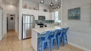 A modern kitchen with a central island, stainless steel appliances, and blue bar stools. - B3 Beach House | Private Pool (Port Aransas)