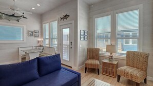 A spacious living room with a blue sofa, wicker chairs, and a dining area with a table and chairs. - B3 Beach House | Private Pool (Port Aransas)
