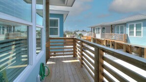 A wooden deck with a railing, a green garden hose, and a view of other buildings. - B3 Beach House | Private Pool (Port Aransas)
