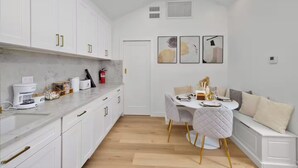 A modern kitchen with white cabinets, a marble countertop, and a dining area with a white table and chairs. - Modern House in Culver City Santa Monica (Culver City)