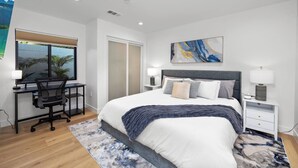 A modern bedroom with a large bed, a desk, and a chair. There is a window with a view of palm trees. - Modern House in Culver City Santa Monica (Culver City)