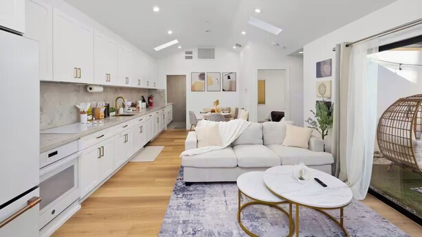 A modern kitchen with white cabinets, a marble countertop, and a dining area with a white sofa and a round table. - Modern House in Culver City Santa Monica (Culver City)