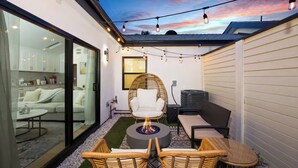A modern patio with wicker furniture, a fire pit, and string lights against a sunset backdrop. - Modern House in Culver City Santa Monica (Culver City)