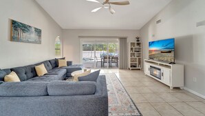A modern living room with a sectional sofa, a flat-screen TV, a ceiling fan, and a fireplace. - Private Pool Oasis near Parks (Port Charlotte)