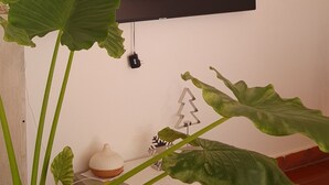 Quarto com televisão de tela plana na parede, um vaso de planta e um objeto decorativo pequeno em um suporte de madeira.