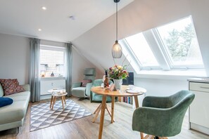 A modern living room with a dining area, a sofa, a coffee table, and a view of the outdoors through a skylight. - Strandkoje Sylt - Central. Quiet. Beach. (Sylt)