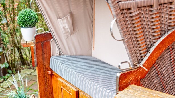 Un espace extérieur accueillant avec un banc rembourré, une chaise en osier et une petite table.