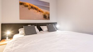 Une chambre à coucher avec un grand lit, une tête de lit et un tableau représentant une scène de plage, accroché au mur.