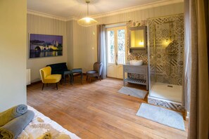 A room with a wooden floor, a bed, a desk, a chair, a small table, a mirror, and a shower area. - Between Mont Ventoux and Luberon, air-conditioned Provencal farmhouse with swimming pool, indoor... (MAZAN)