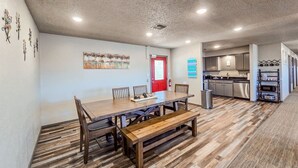 A dining area with a wooden table and benches, a red door, and a kitchen in the background. - Angler Hideaway | Belle Starr Marina | Pool | Fish (Checotah)