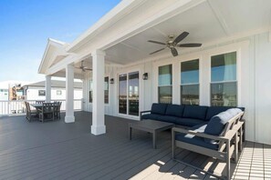 A covered outdoor deck with a sofa and table, large windows, and a ceiling fan. - At The Pointe by Brunswick Vacation Rentals: 4BR 4.5BA w/ Pool, Spa, EV Charger (Ocean Isle Beach)