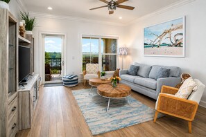A modern living room with a sofa, coffee table, and chairs, a television, and a painting on the wall.
