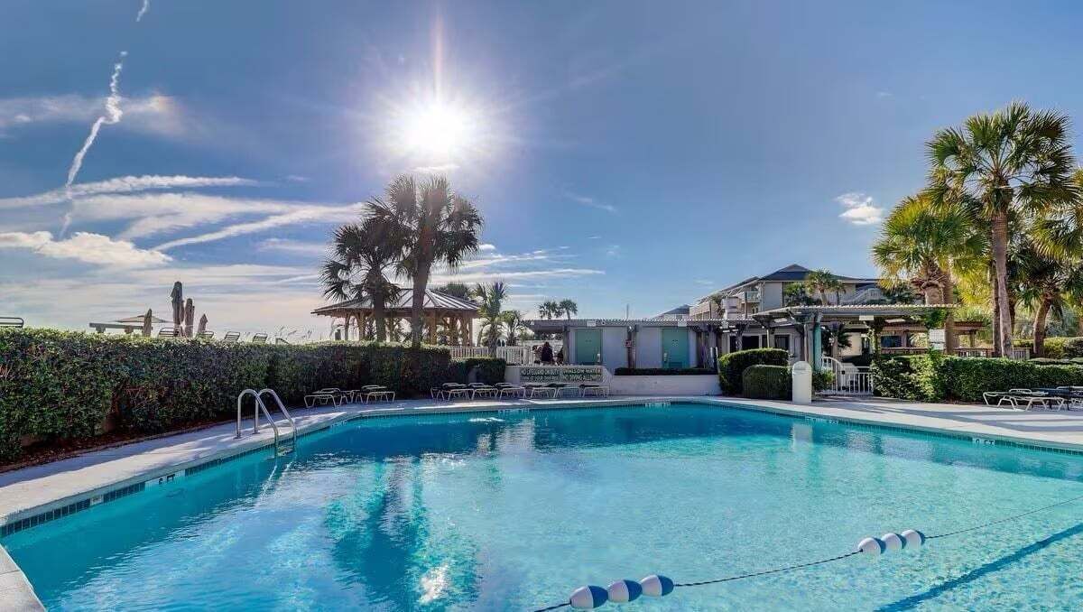 A swimming pool with clear blue water, surrounded by palm trees and lounge chairs.