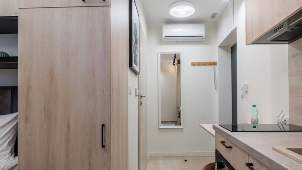 A modern kitchen with wooden cabinets, a built-in oven, and a countertop with a water bottle. - Grunwald Raszyńska Studio (Poznań)