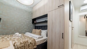 A bedroom with a bed, a wardrobe, a shelf, and a mirror. - Grunwald Raszyńska Studio (Poznań)