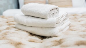 A neatly made bed with a fluffy beige blanket and rolled white towels. - Grunwald Raszyńska Studio (Poznań)
