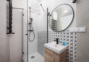 Features a sleek bathroom with a large round mirror, white sink, and geometric tile pattern.